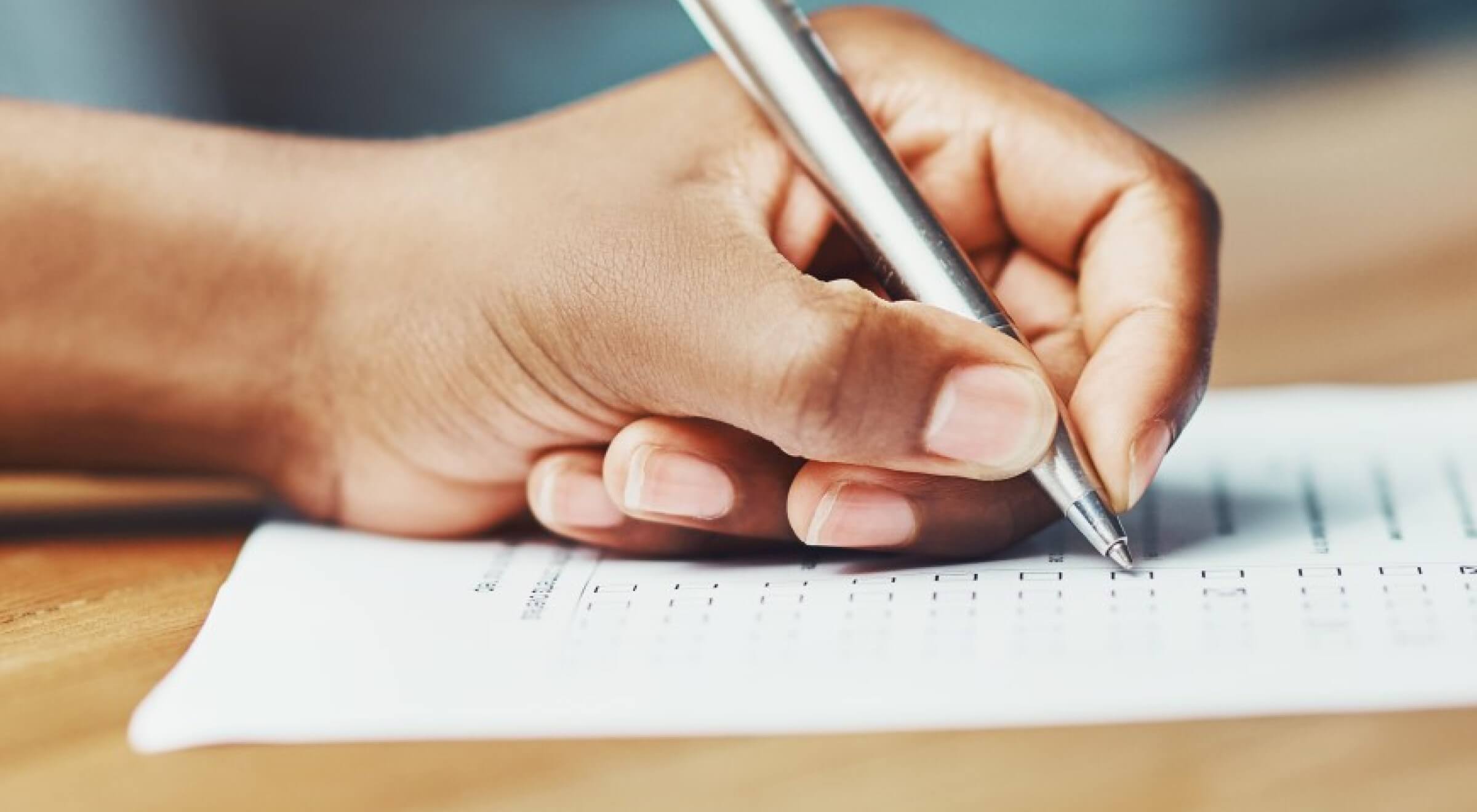A hand writing on a paper with a silver pen