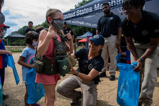 Deputy U.S. Marshal puts tactical vest on child during…